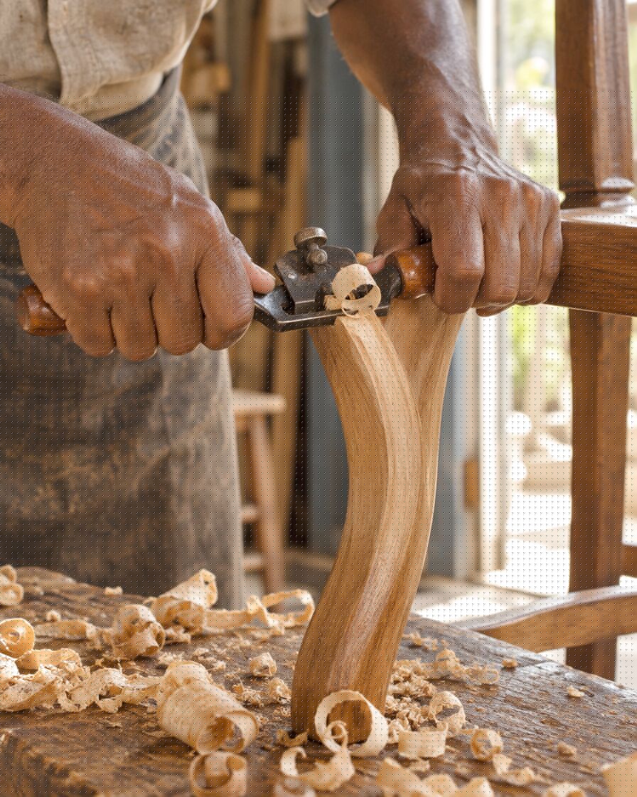 Hands shaping a chair leg with a spokeshave